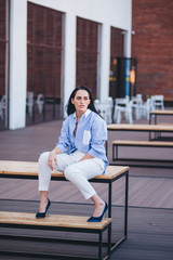 A beautiful woman in a shirt and pants sits on a balcony of a building.