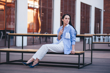 Fototapeta premium A beautiful woman in a shirt and pants sits on a balcony of a building.