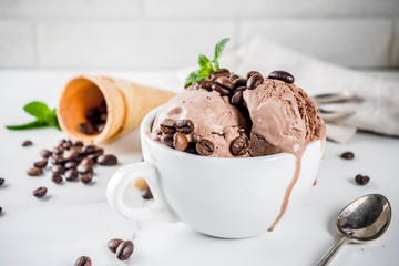 Homemade coffee ice cream, served with coffee beans and mint leaves, with ice cream cones and spoons in the picture. White marble background,