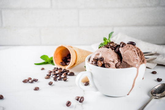 Homemade coffee ice cream, served with coffee beans and mint leaves, with ice cream cones and spoons in the picture. White marble background,