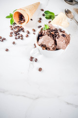 Homemade coffee ice cream, served with coffee beans and mint leaves, with ice cream cones and spoons in the picture. White marble background,