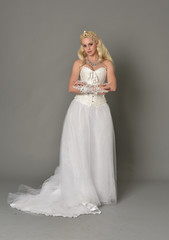 Fototapeta premium full length portrait of blonde girl wearing white corset gown. standing pose on grey studio background.