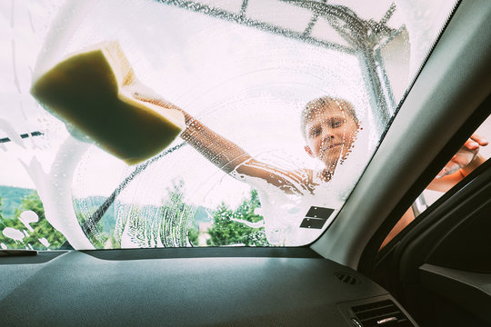 Boy washes front car window with sponge
