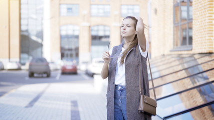 Fototapeta premium A young girl is holding sunglasses outside fixing her hair breathing fresh air outside in the loft zone