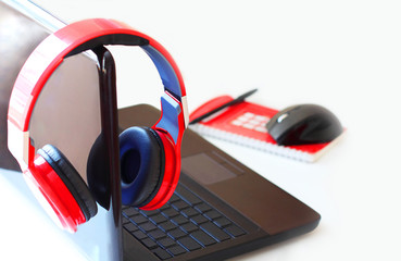 Red headphones and laptop computer, notepad on a light background. Side view. Can be used as a background image to copy space.