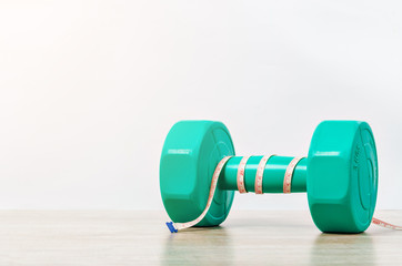 Green dumbbell and measuring tape on wooden background.