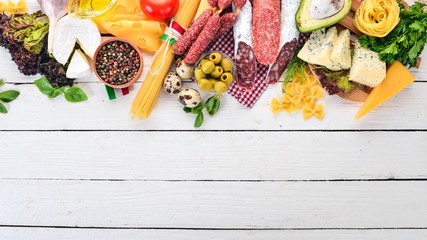 Assortment of sausage, cheese and fresh vegetables. On a white wooden background. Top view. Copy space.