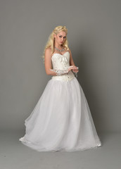 Fototapeta premium full length portrait of blonde girl wearing white corset gown. standing pose on grey studio background.