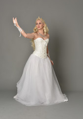 Fototapeta premium full length portrait of blonde girl wearing white corset gown. standing pose on grey studio background.
