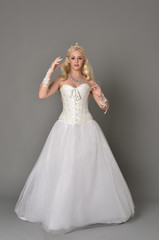 full length portrait of blonde girl wearing white corset gown. standing pose on grey studio background.