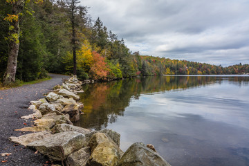 Clouds are reflected in a calm Minnewaska Lake in Orange County, NY, surrounded by bright fall foliage on a partly cloudy afternoon