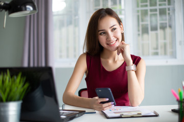 Businesswoman working online using a smart phone sitting in a desktop at office