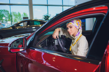 Fototapeta na wymiar property and people concept - muslim woman in hijab with car key over car show background. happy woman taking car key from dealer in auto show or salon