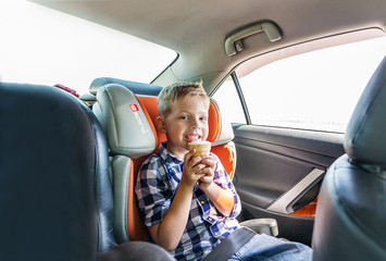 A small boy eating ice cream, sitting strapped in the car seat