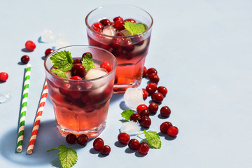 Cranberry cocktail with ice and mint on a blue background, copy space. selective focus.
