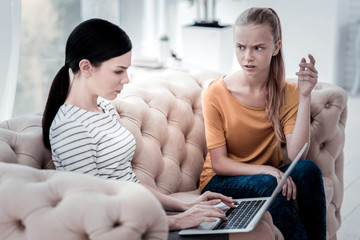 Being confused. Displeased girl sitting on the sofa and expressing irritation while skilled psychologist using a laptop and typing necessary information