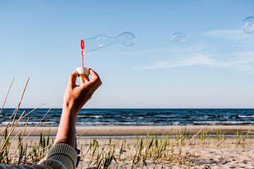 hand of young female playing with soap bubbles outdoors at beach