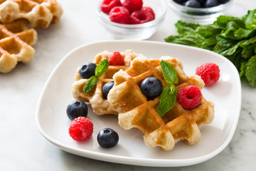 Traditional belgian waffles with blueberries and raspberries on white marble