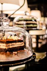 Chocolate cake with mascarpone cream layer under glass bell dome. Cake stand, dessert buffet, storage
