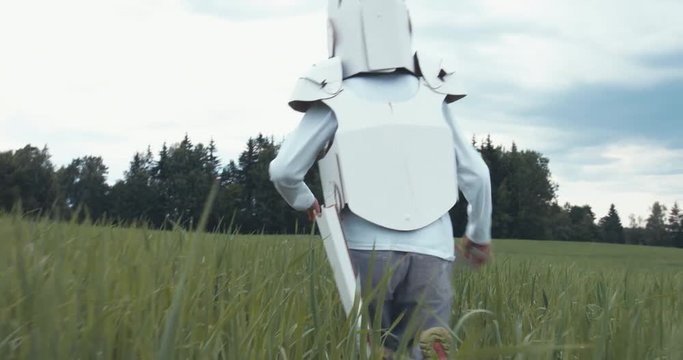 Kid boy wearing cardboard medieval knight armor costume chasing his father pretending to be a dragon in paper mask. 4K UHD 60 FPS SLO MO