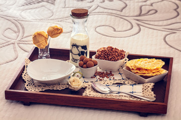 Tray with continental breakfast on hotel bed made of cereals, chocolate, cakes and a bowl with spoon. Breakfast in bed. Front view