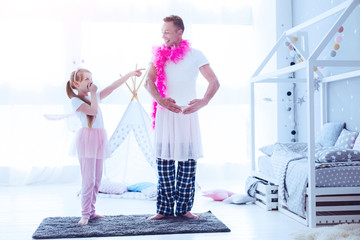 You are so funny. Adorable little kid grinning broadly and pointing toward her loving father wearing a ballerina costume and playing with her.