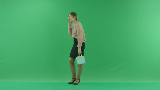 Pretty shopping woman with shopping bags. Female shopper holding shopping bags sideways on green background in studio.