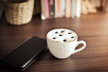 Hot coffee on wooden table with smart phone and pen.