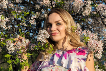 A girl with light wavy hair near blossoming trees in the park