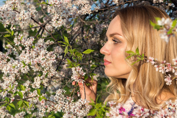 A girl with light wavy hair near blossoming trees in the park