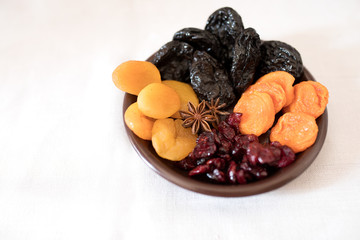 Dried fruits in a bowl. On the plate there are prunes, dried apricots, dried cranberry, dried mooseberry. A white background. View from above. Close-up. Macro photography.