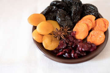 Dried fruits in a bowl. On the plate there are prunes, dried apricots, dried cranberry, dried mooseberry. A white background. View from above. Close-up. Macro photography.