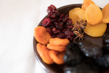 Dried fruits in a bowl. On the plate there are prunes, dried apricots, dried cranberry, dried mooseberry. A white background. View from above. Close-up. Macro photography.