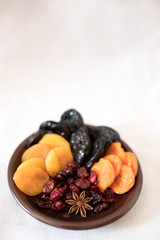 Dried fruits in a bowl. On the plate there are prunes, dried apricots, dried cranberry, dried mooseberry. A white background. View from above. Close-up. Macro photography.