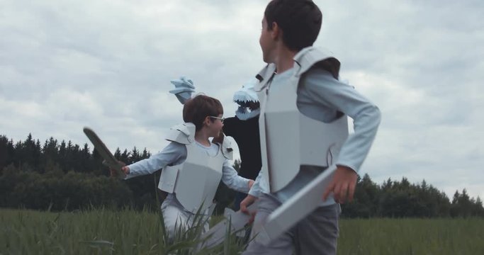 Father pretending to be a dragon in paper mask chasing his sons wearing cardboard medieval knight costumes. 4K UHD 60 FPS SLO MO