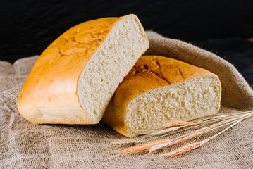 sweet and tasty bread and wheat on black wooden background