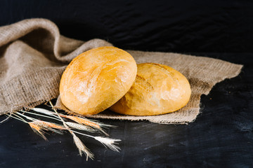 sweet and tasty bread and wheat on black wooden background