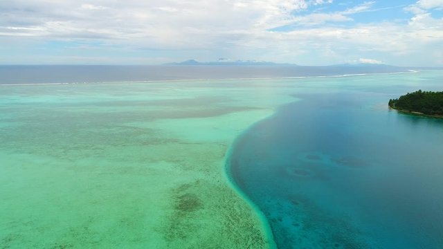 Aerial panoramic view of coral barrier reef around Huahine island, turquoise crystal clear water of blue lagoon, Raiatea and Tahaa on horizon - South Pacific Ocean, seascape of French Polynesia, 4k
