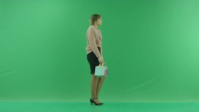 Pretty shopping woman is dancing with shopping bags. Female shopper holding shopping bags sideways on green background in studio.
