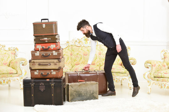 Macho elegant on strict face carries vintage suitcase. Man, butler with beard and mustache wearing classic suit delivers luggage, luxury white interior background. Luggage and relocation concept.