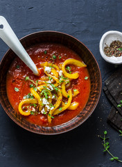 Tomatoes soup with roasted bell yellow pepper and goat cheese. Delicious vegetarian food on dark background, top view