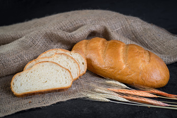 Sweet tasty bread and wheat on wooden background