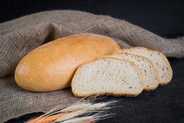 Sweet tasty bread and wheat on wooden background