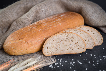 Sweet tasty bread and wheat on wooden background