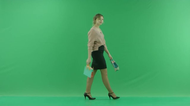 Pretty shopping woman is walking with shopping bags. Female shopper holding shopping bags front on green background in studio.