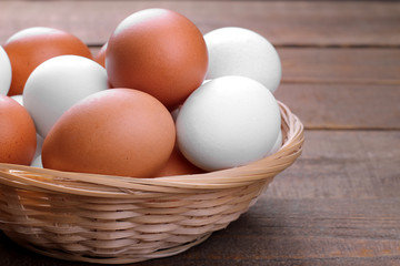 Brown and white chicken eggs in a wicker basket on a brown wooden background.