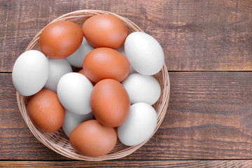Brown and white chicken eggs in a wicker basket on a brown wooden background. Top view