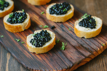 Black caviar on the pieces of bread over wooden kitchen board.