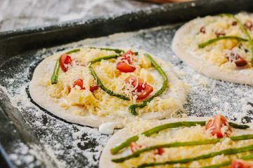 Cooking process of making mini pizza - small and personal, with cheese, tomatoes and asparagus.