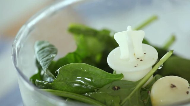 Chef adds oil into the blender with spinach.